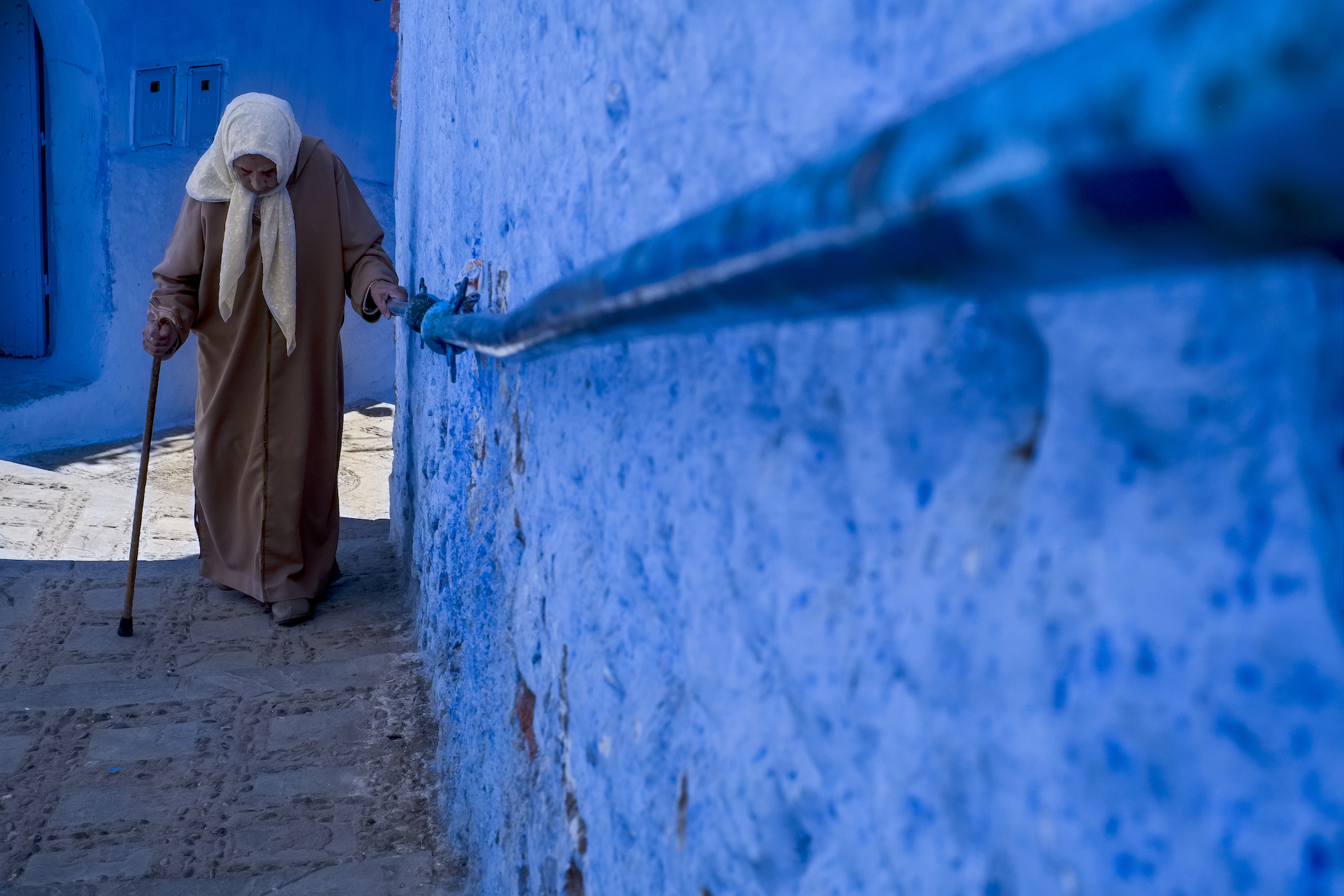 An elderly lady climbing steps in Chafchaouen, Morocco, by Laurie Cohen.